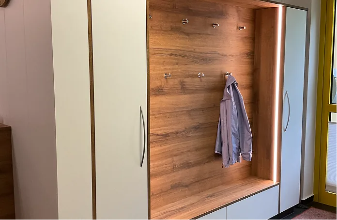 Ein Flur mit einem Holzgarderobenschrank mit weißen Türen und einer Jacke an einem Haken.