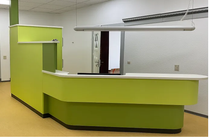Grüner Empfangstresen mit weißer Arbeitsfläche in einem Büro mit weißer Wand.