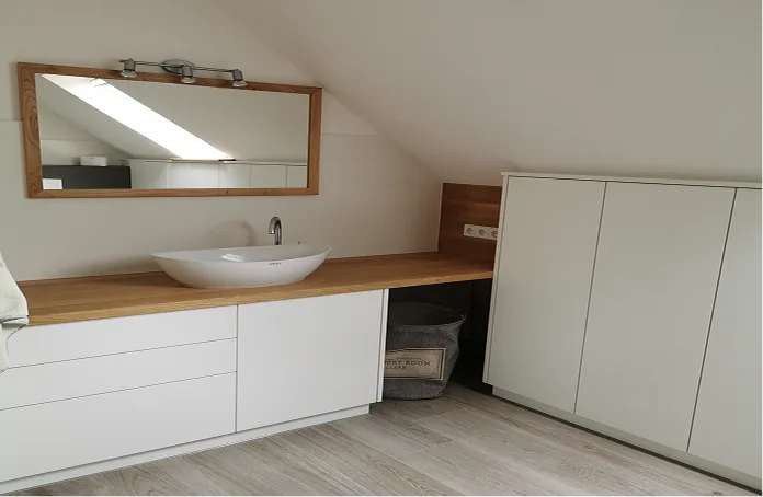 Modernes Waschbecken mit Holzarbeitsplatte, großem Spiegel und weißen Schränken unter der Dachschräge.