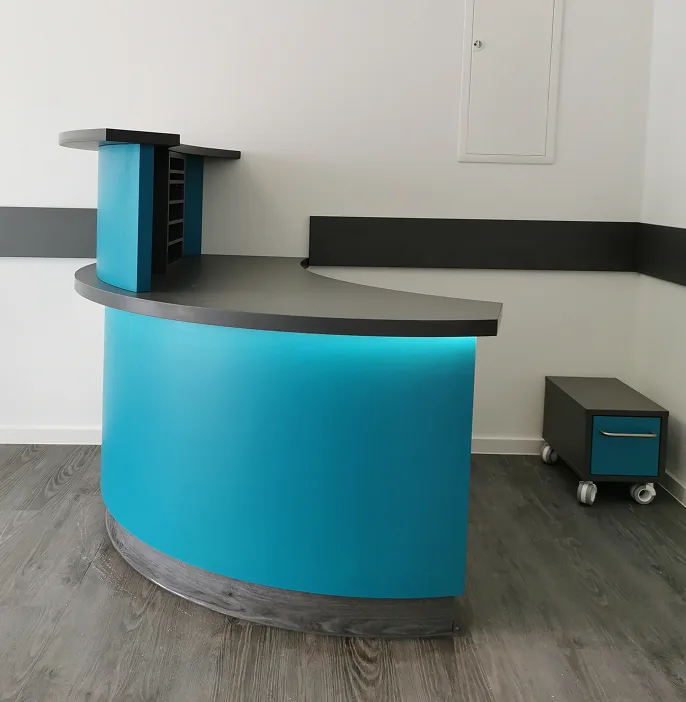 Blauer Empfangstresen mit schwarzer Arbeitsfläche und einem kleinen rollbaren Schrank neben weißer Wand.