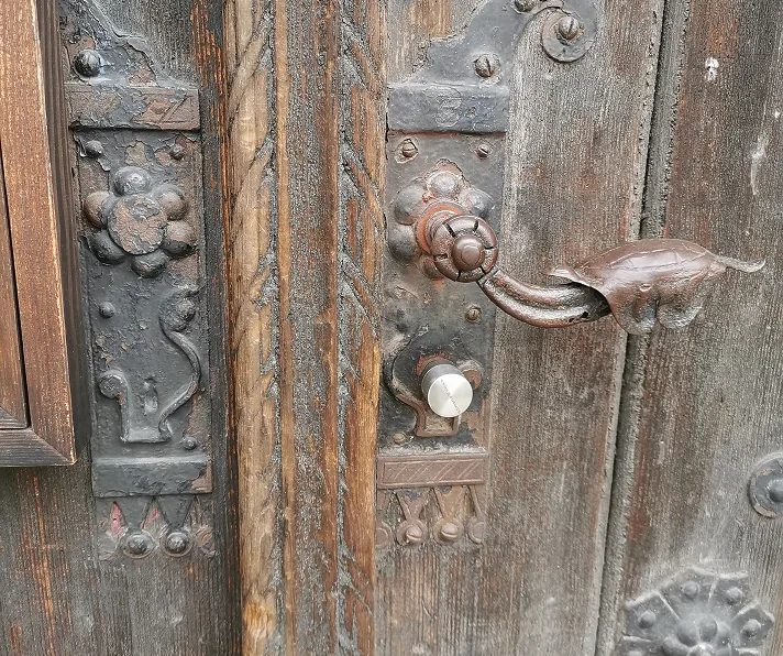 Detail einer alten Holztür mit einem verzierten Türgriff und Metallbeschlägen.