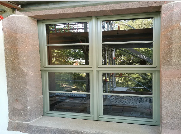 Grünes Fenster mit vier geteilten Scheiben in einem steinernen Fensterrahmen.