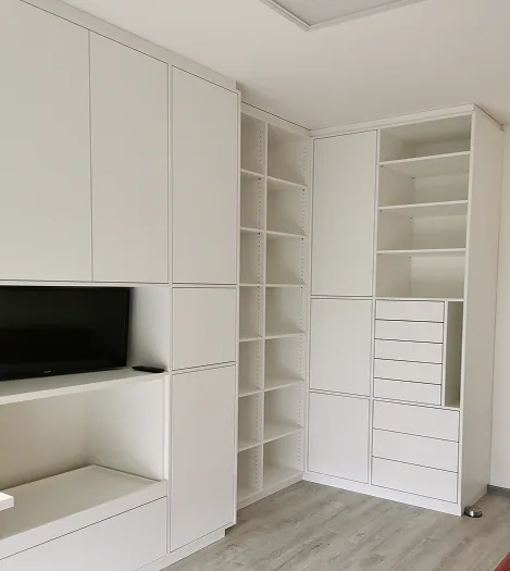 Weißes, modernes Regal- und Schranksystem mit Fernseher und offenen Regalen in einem Raum.