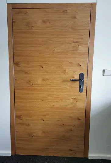 Ein geschlossener Glastürflügel mit Holzdekor und metallischem Türgriff an weißer Wand.