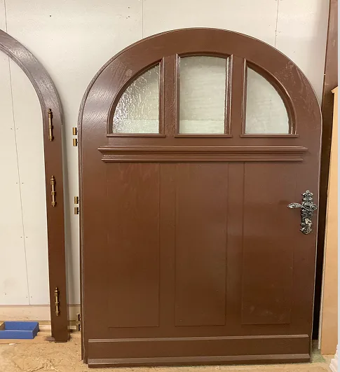 Braune Holztür mit drei halbkreisförmigen Fensterabschnitten und silbernem Griff.
