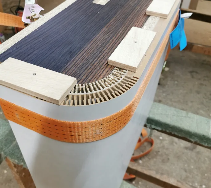 Nahaufnahme einer geschwungenen Holzkante mit Furnierschichten und oranger Kante.